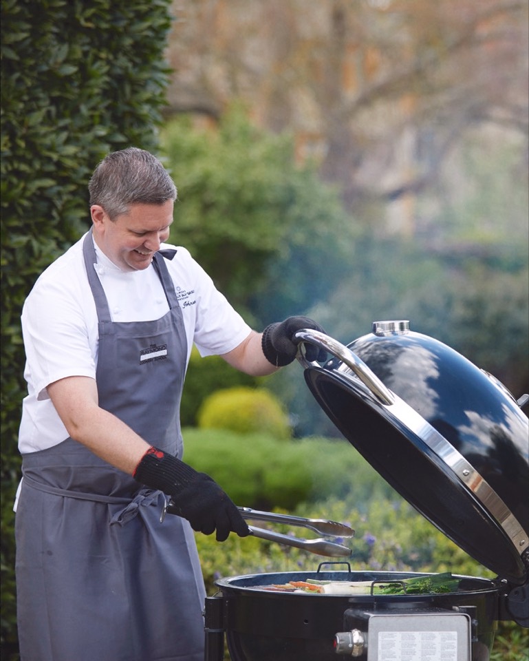 Adam Johnson cooking over a live-fire barbecue in chef whites