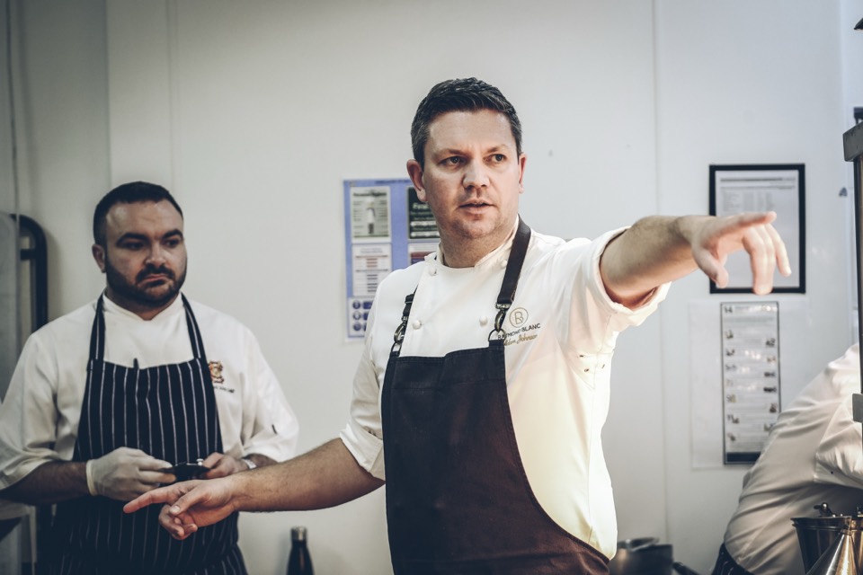 Adam Johnson directing a kitchen team in chef whites